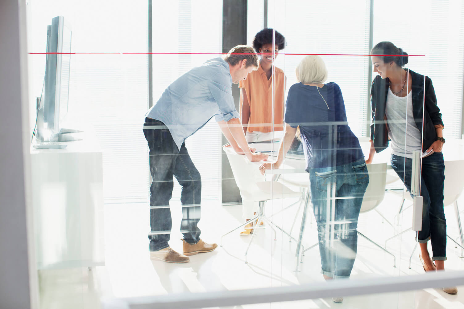 A group of four people gathered around a table, engaged in a collaborative discussion in a bright, modern office setting.