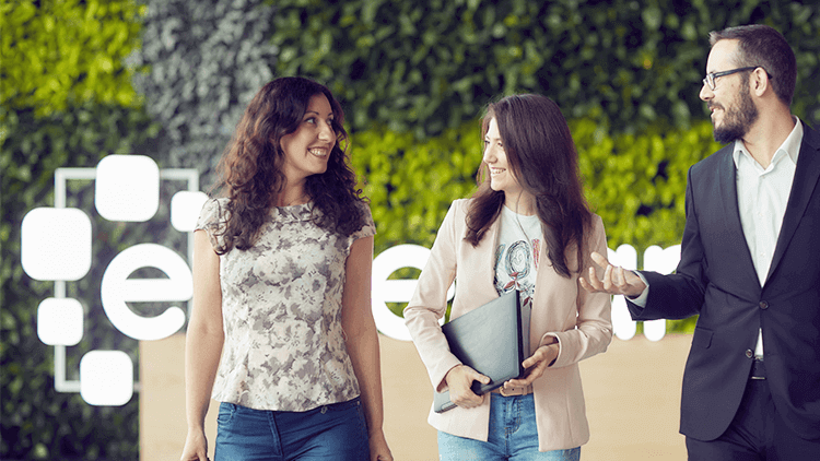 Two caucasian females and one caucasian male walking and talking with a lit up Experian logo in the background.