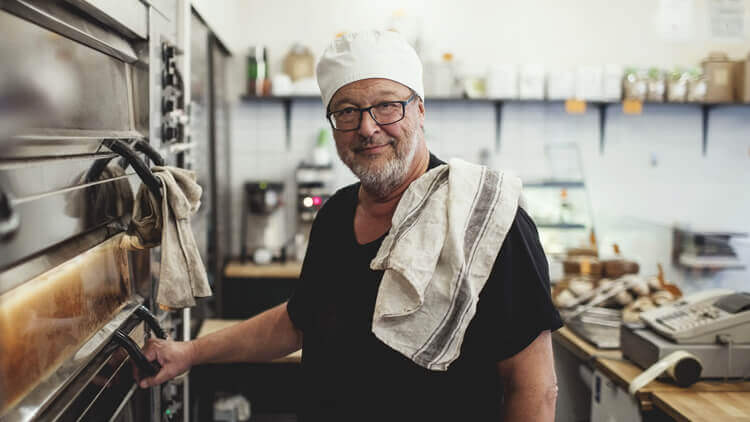 Male chef stood in the kitchen in front of the oven, looking into the camera 