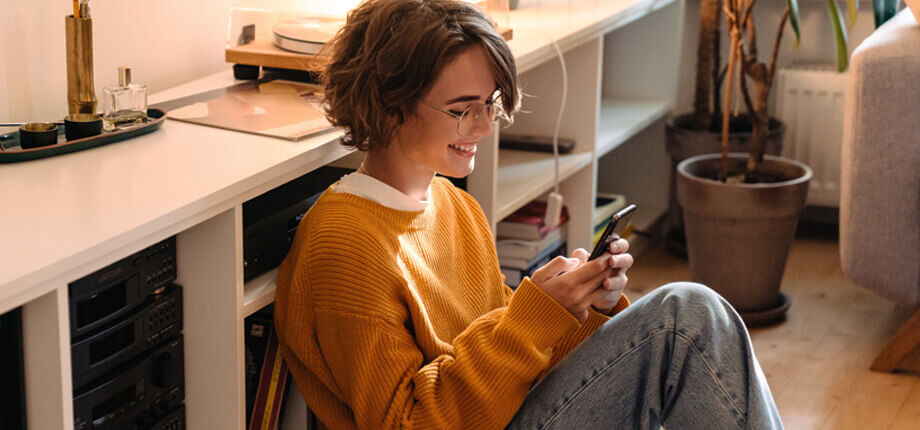 Woman sat on the floor at home smiling looking at her phone