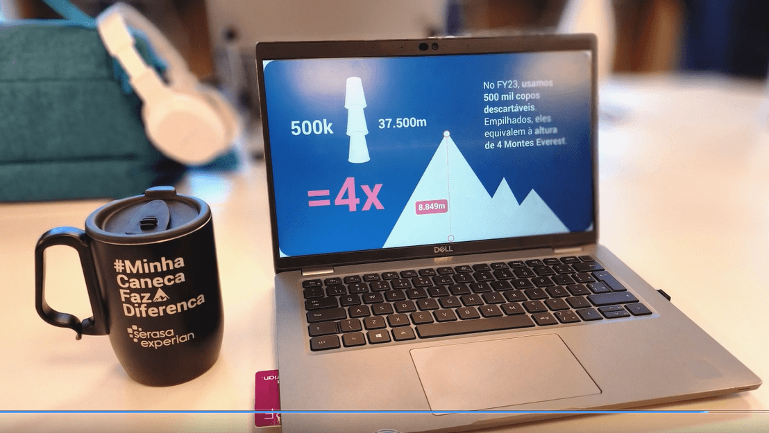 Photo of a reusable branded mug on a desk next to a laptop