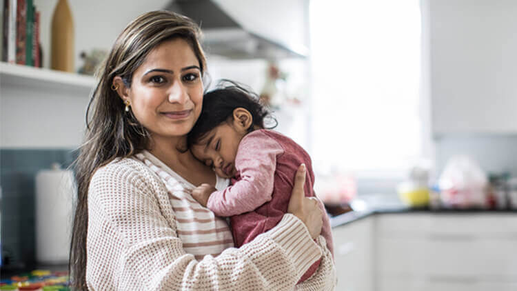 Mother holding her daughter in her arms stood in the kitchen 